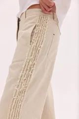 Pantalón de lino lavado color beige, de calce recto y diseño relajado. Presenta cintas de lino desflecadas aplicadas en los laterales con pespunte central, pretina con botón metálico, bolsillos delanteros y traseros.