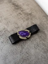 Cinturón de cuero negro con hebilla metálica grande y piedra de ágata violeta en el centro.