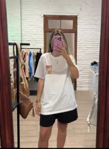 Remera blanca de algodón, corte oversize y manga corta, con un pequeño bolsillo estampado en el pecho con diseño de frutas y texto.