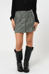 Minifalda gris con textura símil cuero, corte irregular con sobrefalda y cierre frontal con broches metálicos.