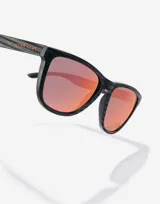 Gafas de sol unisex Hawkers edición limitada Alex Rins, con montura cuadrada negra con textura de fibra de carbono y lentes polarizadas color naranja.