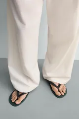 Sandalia tipo ojota o chancleta de goma, con base de color verde oscuro y tiras negras. Presenta una suela plana.