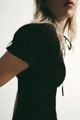 Top marrón de tejido texturizado con cuello redondo, lazada frontal y escote en pico. Presenta mangas cortas abullonadas con terminación elástica, cuerpo con estructura tipo nido de abeja y cierre frontal con botones.