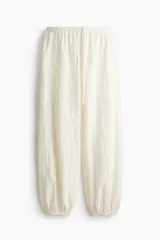 Pantalón blanco de punto con diseño texturizado estilo encaje, de corte holgado con piernas globo, cintura elástica con cordón ajustable y bajos con elástico.