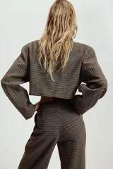 Blazer corta de corte recto con estampado de cuadros pequeños en tonos marrones y negros. Presenta cuello solapa, manga larga y cierre frontal con un botón.