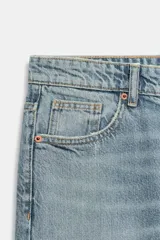 Jeans de tiro medio con corte relajado y diseño de cinco bolsillos. Presenta trabillas en la cintura, cierre frontal con cremallera y botón metálico, con un acabado de lavado desgastado.