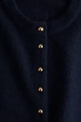 Buzo de punto suave color azul marino, con cuello redondo y abertura frontal con botones dorados. Presenta hombros caídos y puños y bajo en punto acanalado.