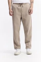 Pantalón de jogging color beige, confeccionado en algodón y poliéster, con cintura elástica y cordón ajustable. Diseño clásico sin puño en los tobillos.