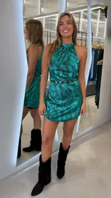 Vestido corto color verde con acabado metalizado y efecto plisado, cuello halter y diseño sin mangas. Incluye un cinturón delgado con hebillas metálicas.