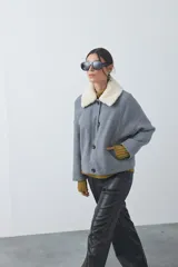 Campera corta de paño color gris con cuello de corderito blanco, cierre frontal con botones y bolsillos laterales.