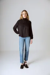 Blusa negra de manga larga con cuello alto fruncido y diseño amplio con frunces en la parte superior.