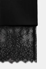 Vestido tipo blazer negro, de corte recto y largo medio, con cuello solapa, manga larga con abertura y botones, y bolsillos con solapa en el delantero. Presenta un bajo con aplicación de encaje negro a tono.