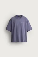 Camiseta relaxed fit de color gris con efecto lavado, cuello redondo y manga corta. Cuenta con un pequeño texto estampado en contraste en el pecho.