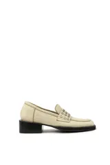 Mocasín color marfil de cuero, con detalle de tachas plateadas en la parte delantera y suela de goma negra.