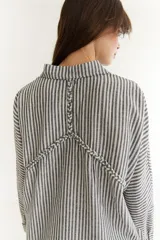 Camisa de corte oversize color bordó, con cuello clásico, cierre frontal de botones y detalle de trenzado horizontal en la parte superior delantera. Posee mangas largas con puños abotonados.