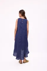 Vestido largo color beige, sin mangas, con escote redondo y abertura en forma de gota en el pecho. Tiene corte holgado y ruedo con volantes.