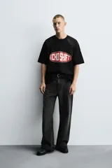 Camiseta negra de corte boxy fit con paneles laterales y de hombros en tejido de malla. Presenta un estampado frontal ovalado con borde rojo y texto blanco que dice "ECHO SHIFT".