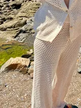 Conjunto de dos piezas compuesto por un cárdigan de botones y un pantalón de corte recto, ambos confeccionados en tejido de punto calado color manteca.