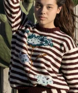 Sweater artesanal de punto tejido a mano en 100% lana merino, con diseño de rayas horizontales en color bordó y crudo, y detalle de diseño floral bordado en la parte frontal.