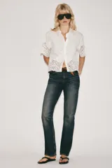 Camisa blanca de manga corta y cuello solapa, con detalles de bordados perforados y encaje en el borde inferior y las mangas. Cuenta con cierre frontal de botones.