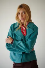 Chaqueta de paño color gris oscuro, con solapas amplias y cierre frontal mediante un alamar único. Presenta bolsillos laterales y mangas largas con puños rectos.