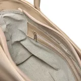 Cartera grande tipo tote bag de cuero color beige claro, con textura granulada. Presenta dos asas de hombro fijas y un diseño con pliegues verticales a los lados. Tiene cierre principal y bolsillo interno con cierre.