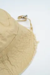 Gorro tipo bucket color verde, con ala ancha y bordes deshilachados. Incluye una pequeña hebilla metálica decorativa en el lateral.