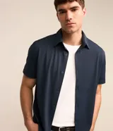 Camisa de manga corta azul marino, de corte recto con cuello camisero y cierre frontal de botones.