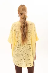 Camisa de broderie color amarillo, con silueta oversize, escote en V, cierre frontal con botones y mangas 3/4. Presenta un diseño con bajo asimétrico, siendo más larga en la parte posterior.