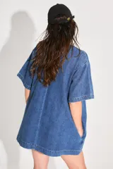 Vestido corto de denim azul con corte holgado, mangas cortas y bolsillo frontal con logo bordado. Cuenta con cierre metálico en la espalda.