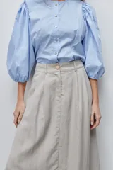 Falda midi color beige de tiro alto y silueta amplia, confeccionada en tela liviana con pinzas en el frente, pasacintos y bolsillos laterales.