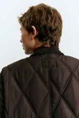 Campera de tejido guateado con diseño de rombos, cuello redondo acanalado, cierre frontal con botones a presión y bolsillos laterales. Presenta ribetes en los bordes y forro interior.