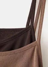 Vestido corto marrón con efecto de doble prenda, superpuesto sobre un fondo negro. Presenta tirantes finos y un diseño ajustado al cuerpo con fruncidos en los laterales.