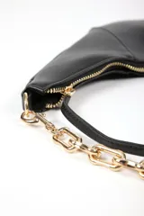 Cartera tipo media luna color negro, con textura granulada y correa de cadena dorada. Tiene cierre de cremallera y un tirador con flecos.