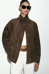 Chaqueta de tejido efecto ante color marrón, con cuello alto, cierre frontal con cremallera y botones a presión, manga larga y bolsillos de plastrón con solapa en el delantero.