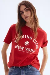 Remera de algodón color rojo, con cuello redondo y manga corta. Presenta un estampado frontal en blanco con el texto "Running Club New York Central Park - Manhattan" y un logo circular con una 'R' en el centro.