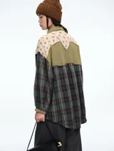 Camisa de corte oversize con diseño patchwork que combina paneles de tela a cuadros en tonos oscuros con paneles superiores de tela beige con estampado floral. Presenta cierre frontal con botones, cuello clásico y bolsillos delanteros con solapa.