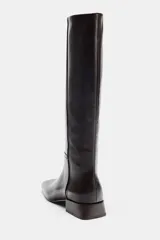 Bota de piel color marrón oscuro, de caña alta, con detalle de pespuntes en el cuerpo, tacón medio en bloque y punta cuadrada.