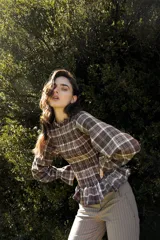 Blusa de tela cuadrillé en tonos tierra, con cuerpo fruncido tipo smock, mangas abullonadas y detalles de volados en el cuello y la cintura.