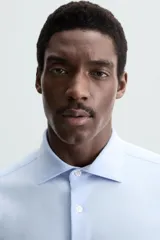 Camisa de manga larga, color celeste con finas rayas verticales blancas, cuello italiano y cierre frontal de botones.