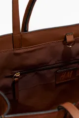Cartera tote color marrón con doble asa de mano y correas finas para el hombro. Cuenta con cierre de mosquetón en el interior y un compartimento interior con cierre.