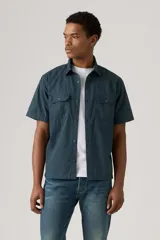Camisa de manga corta color azul petróleo, con cuello clásico, cierre frontal con botones, dos bolsillos de parche con botón en el pecho y corte recto.