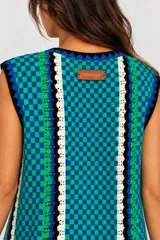Vestido corto de tejido tipo crochet con diseño de damero en tonos azul y verde, escote en V con cordones negros para ajustar y detalles en blanco y negro.