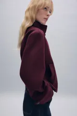 Abrigo corto de paño con mezcla de lana, color bordó. Presenta cuello subido, cierre frontal cruzado con botones, mangas largas con trabillas decorativas y bolsillos laterales de vivo.