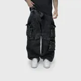 Pantalón tipo cargo de corte ultra baggy, confeccionado en denim de algodón con efecto lavado. Presenta múltiples bolsillos laterales con solapa y cierre de botones, diseño de tiro medio y pernera ancha.