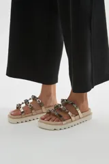 Sandalias chatitas color tostado con dos tiras cruzadas decoradas con tachas metálicas semiesféricas. Suela track de plataforma baja.