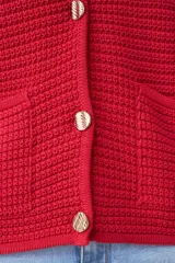 Chaqueta de punto color rojo, de corte entallado y manga larga. Presenta cuello redondo y cierre frontal con botones metálicos dorados texturizados.