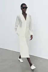 Camisa de mujer fluida de ZARA WOMAN COLLECTION, confeccionada en hilatura con mezcla de lyocell. Presenta escote en pico, manga larga con puños marcados y bajo asimétrico, con cierre frontal de botones ocultos.