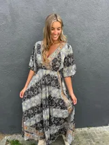 Vestido largo de seda con estampado geométrico y tribal en tonos negros, grises y marrones, escote en V cruzado y mangas fluidas tres cuartos.