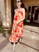 Vestido largo de lino con estampado tie-dye en tonos naranja, rojo y amarillo. Tiene breteles finos y volados en el ruedo.